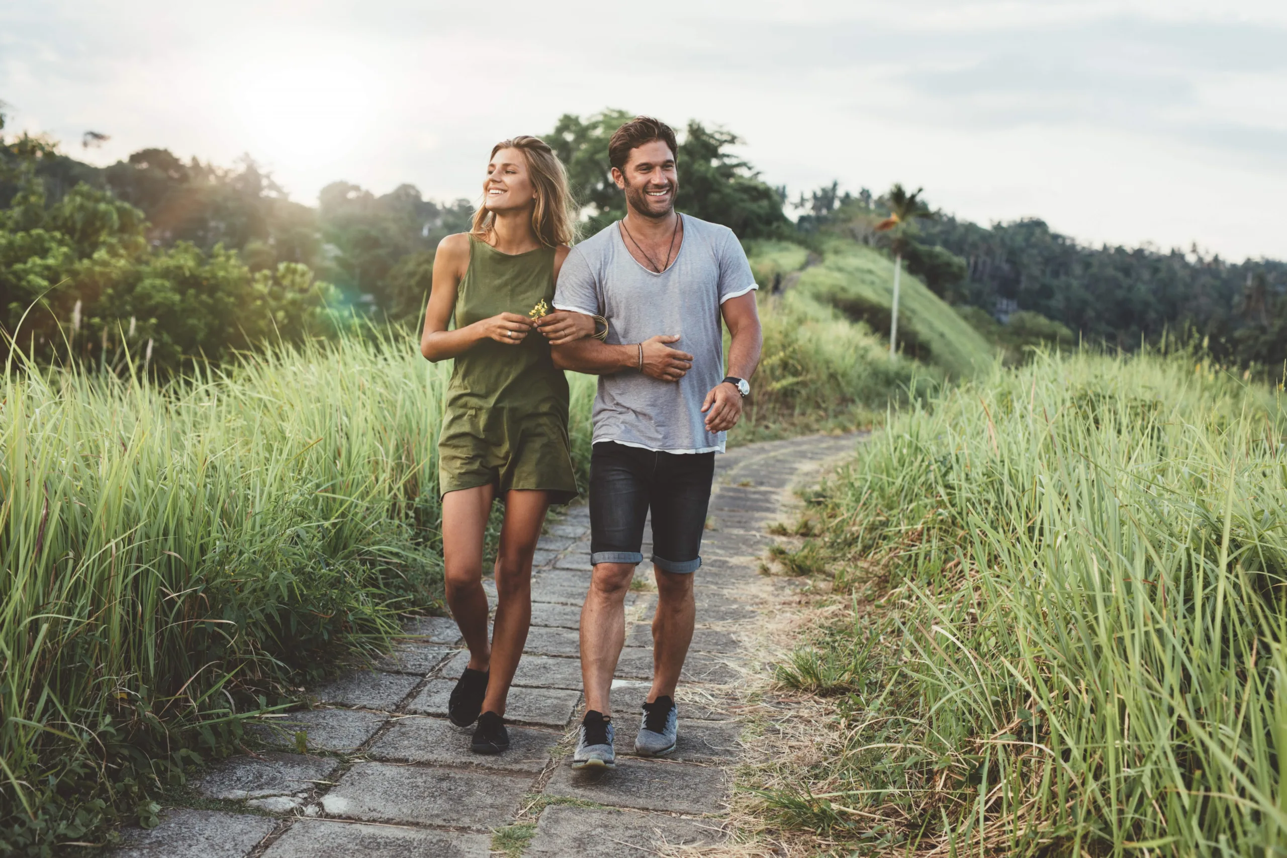 Couple walking through a path beside tall grass on a warm sunny day smiling.